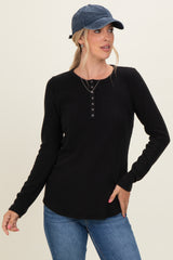 woman wearing a black long sleeve henley top with button details and a blue cap, paired with jeans