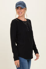woman wearing a black long sleeve henley top with buttons, paired with blue jeans and a blue cap