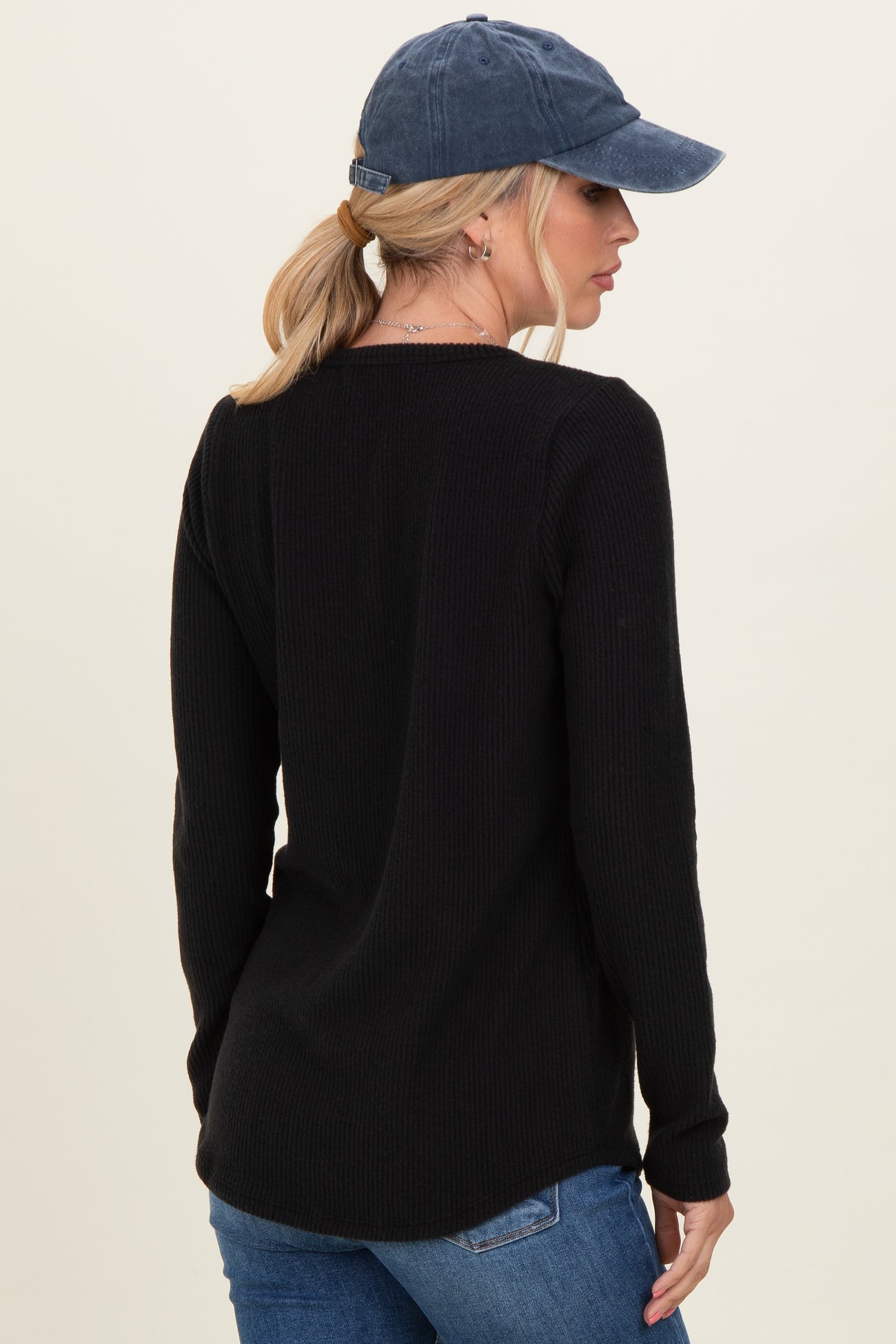 woman wearing a black ribbed long sleeve top and blue baseball cap, showing the back view