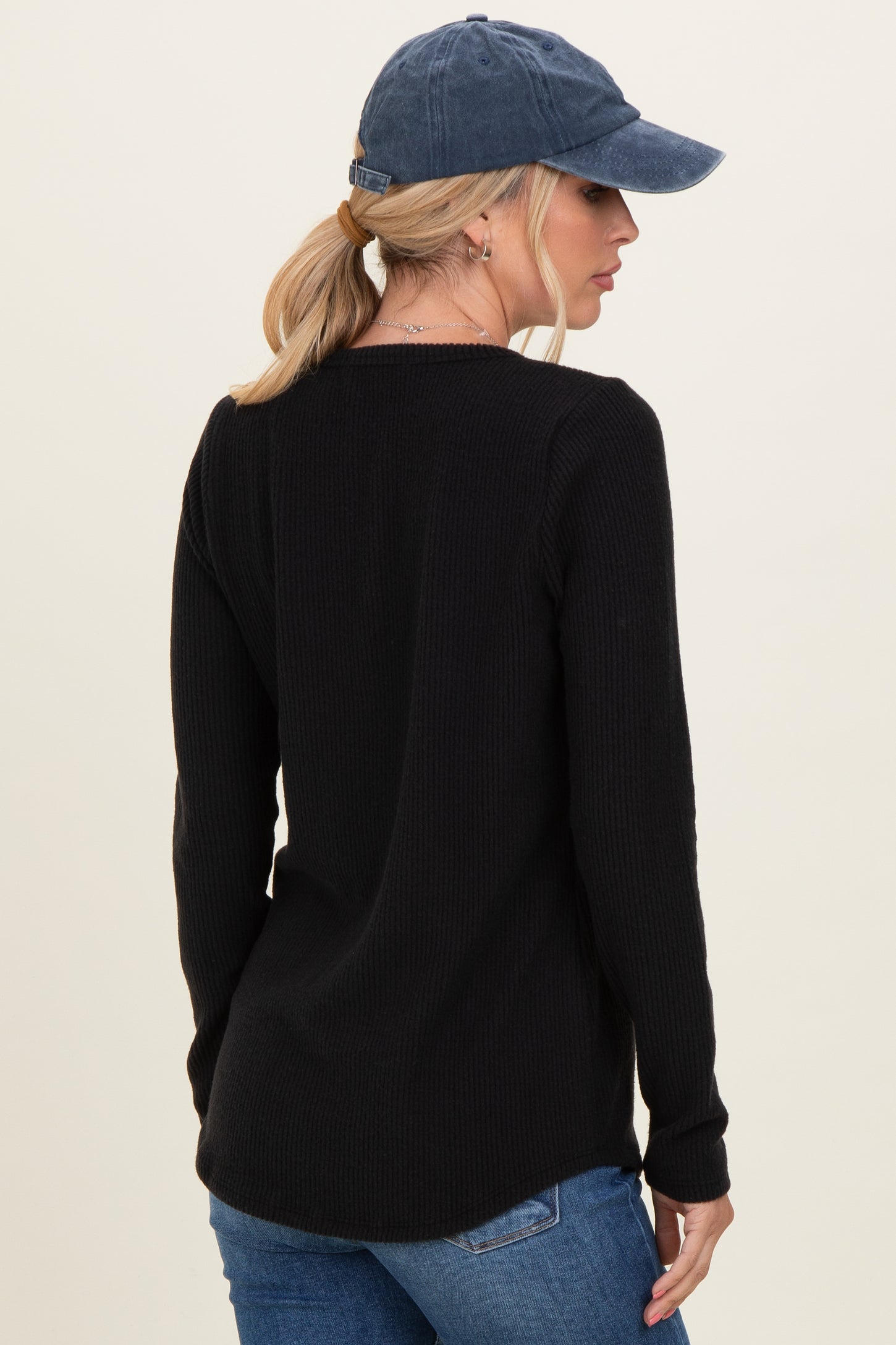 woman wearing a black ribbed long sleeve top and blue baseball cap, showing the back view
