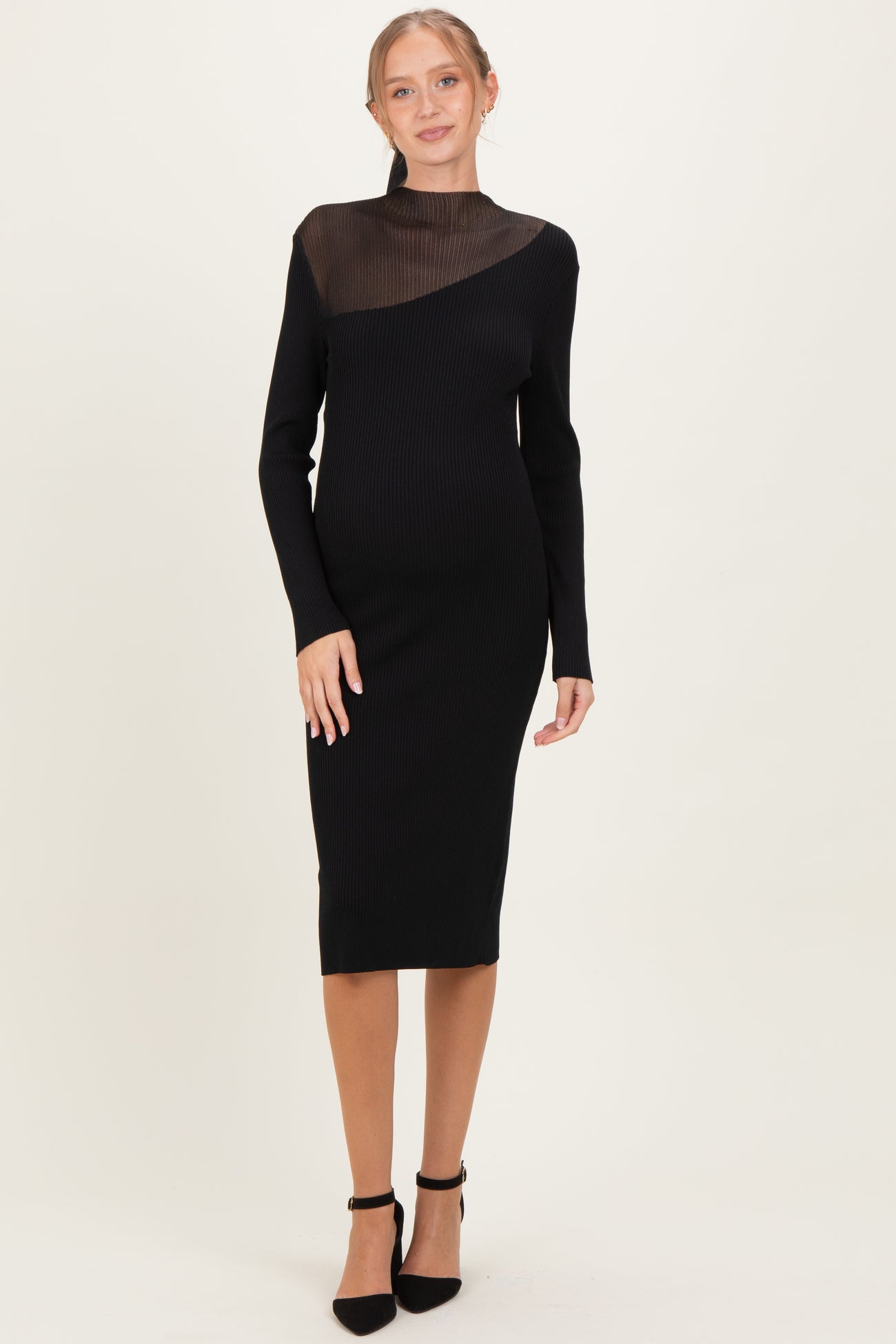woman wearing a black ribbed maternity dress with a sheer mesh panel and long sleeves, showcasing her baby bump