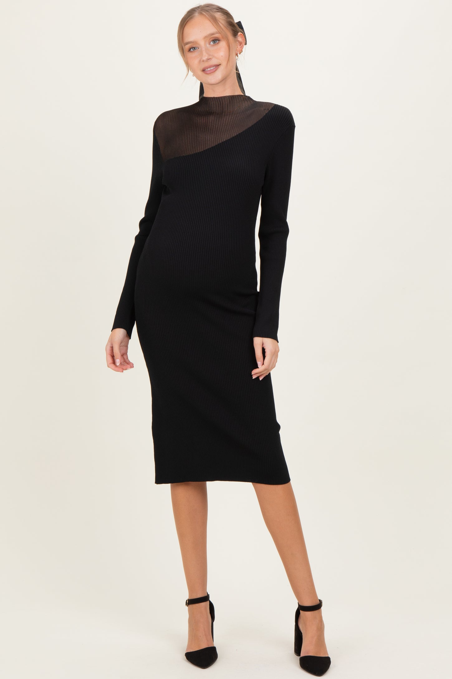 woman wearing a black ribbed maternity dress with a sheer mesh detail at the neckline and long sleeves, showing a baby bump