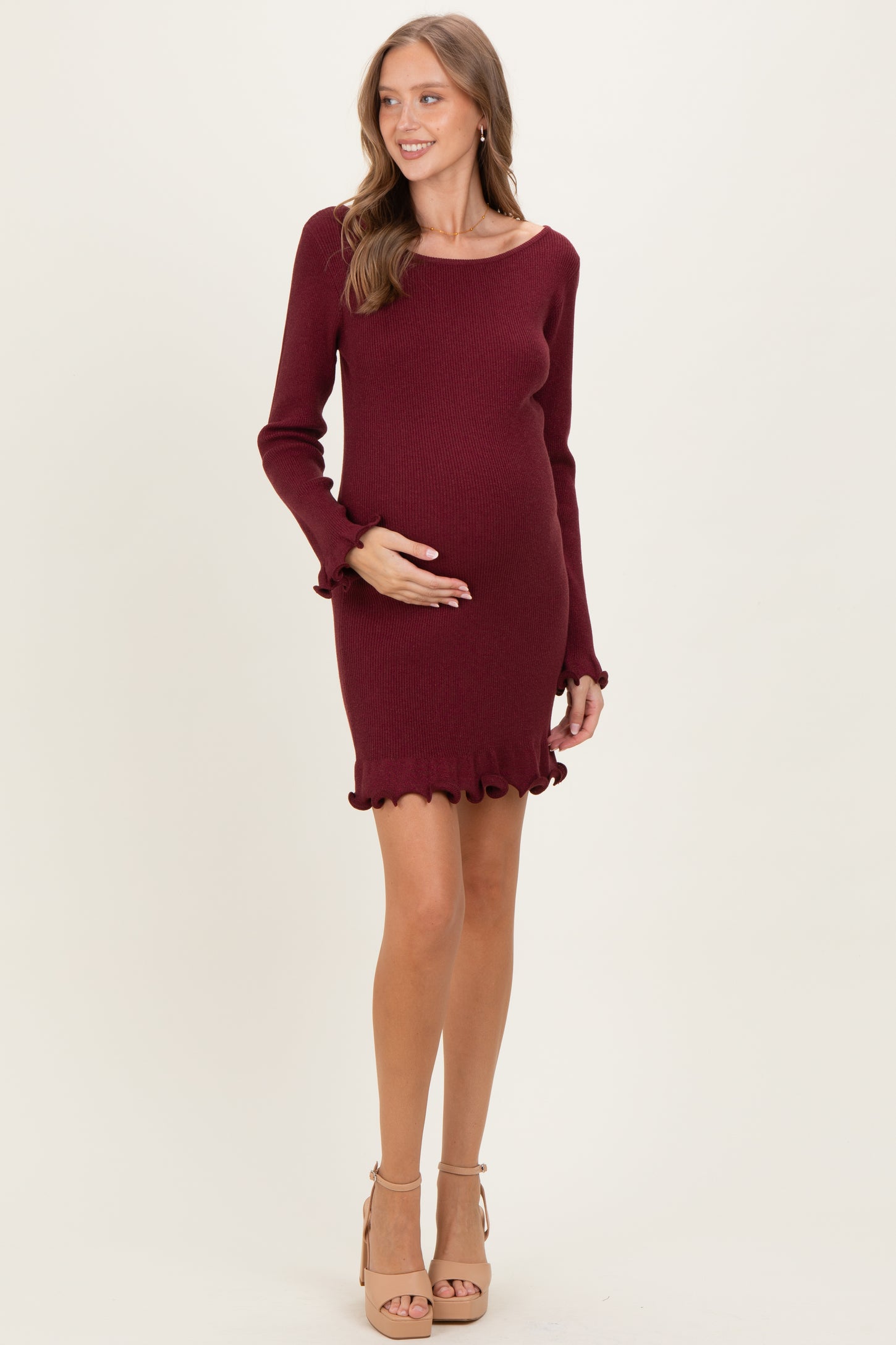 woman wearing a burgundy long sleeve maternity dress with ruffle hem and holding her baby bump