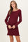 woman wearing a burgundy ribbed long sleeve maternity dress with ruffle hem and holding her baby bump