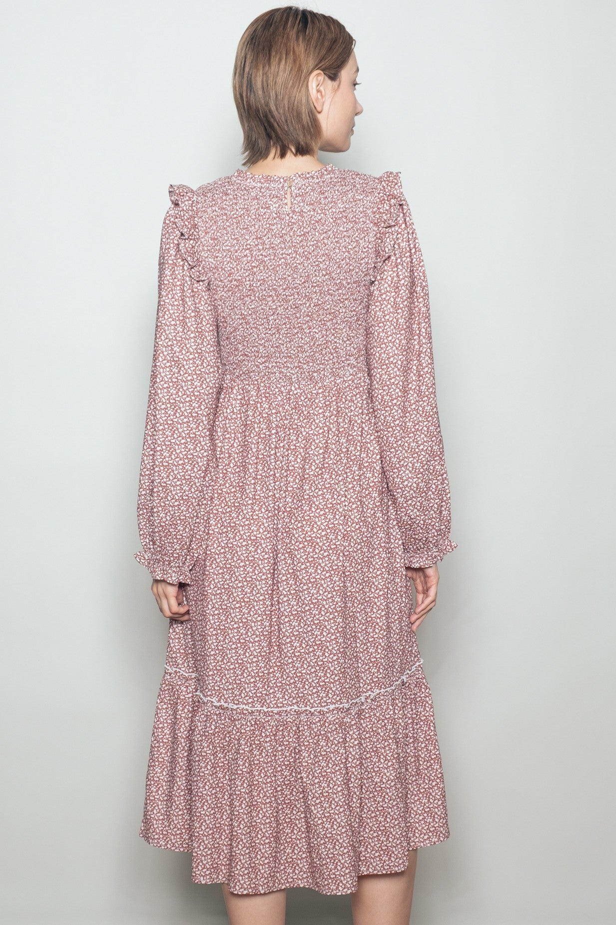 woman wearing a maroon floral long sleeve dress with ruffle details and a tiered skirt seen from the back