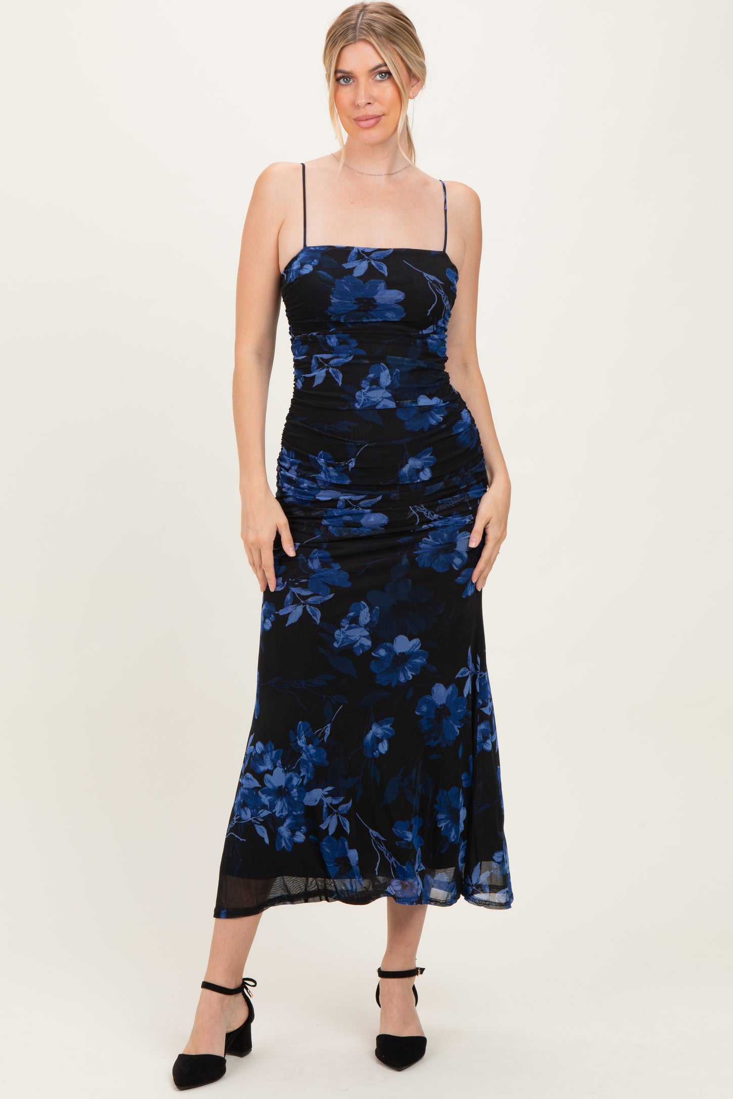 woman wearing a black floral midi dress with blue flowers and spaghetti straps, posing confidently