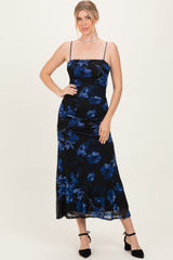 woman wearing a black floral maxi dress with blue flowers and adjustable spaghetti straps, posing with one hand on hip