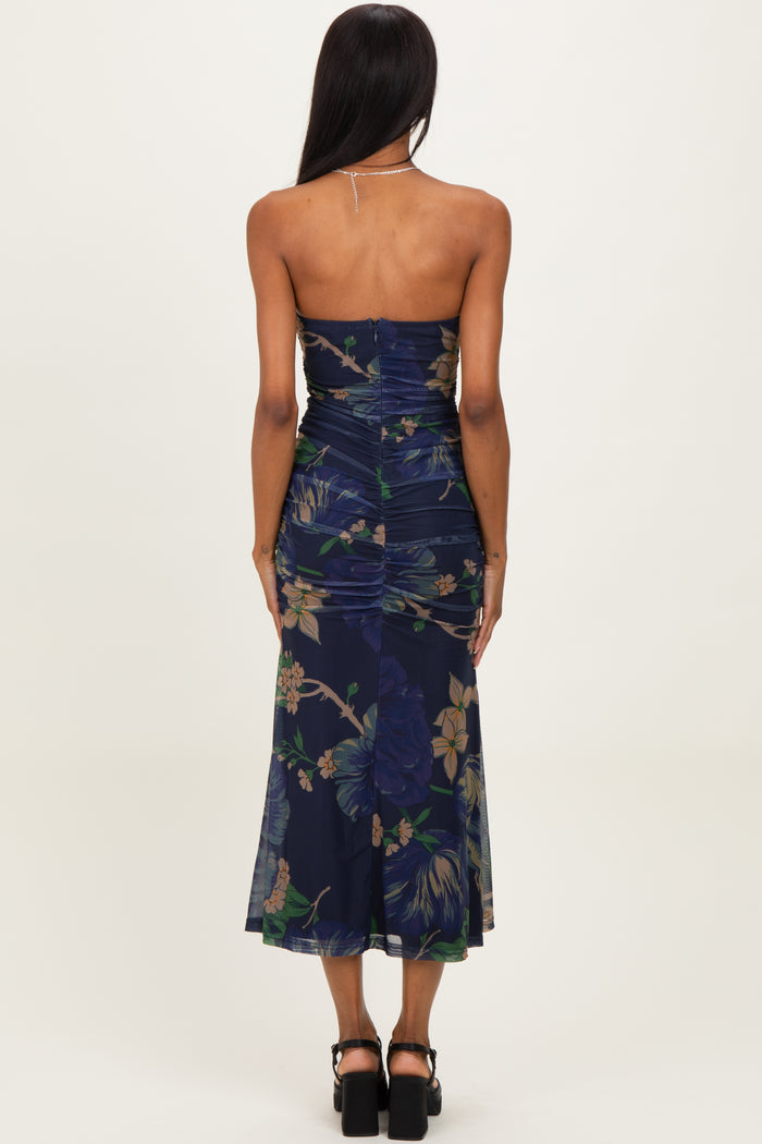 woman wearing a dark floral strapless midi dress with ruching and a flowing skirt, viewed from the back