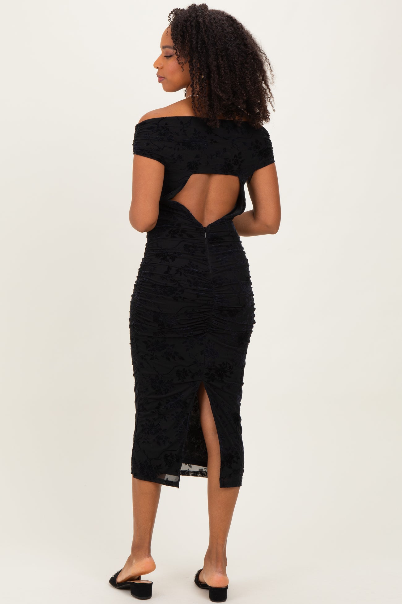 woman wearing a black off-the-shoulder midi dress with a back cutout and ruching details