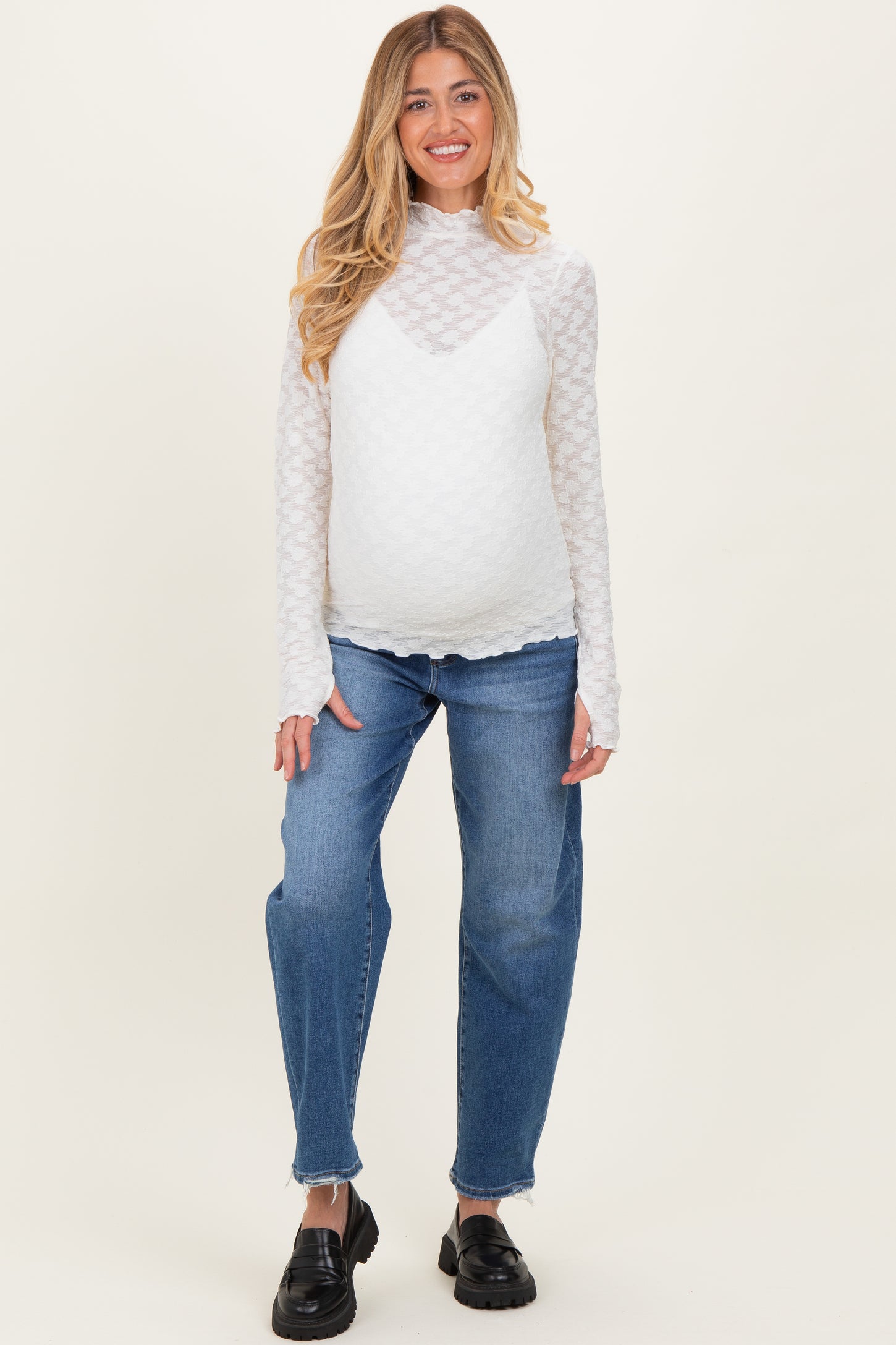 woman wearing a white long sleeve maternity top with textured pattern and blue maternity jeans, showing her baby bump