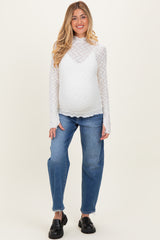 woman wearing a white long sleeve maternity top with textured pattern and blue maternity jeans, showing her baby bump