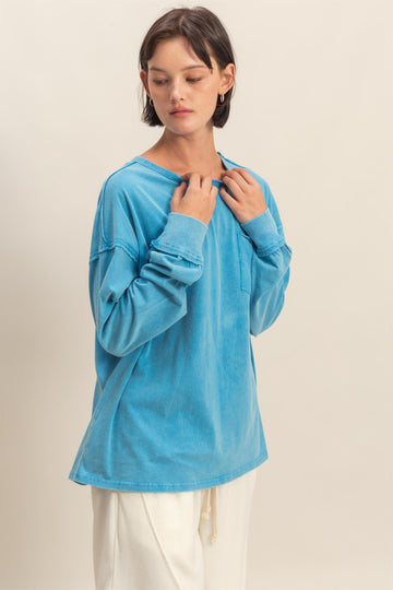 woman wearing a light blue long sleeve oversized top with a pocket, styled with cream-colored pants