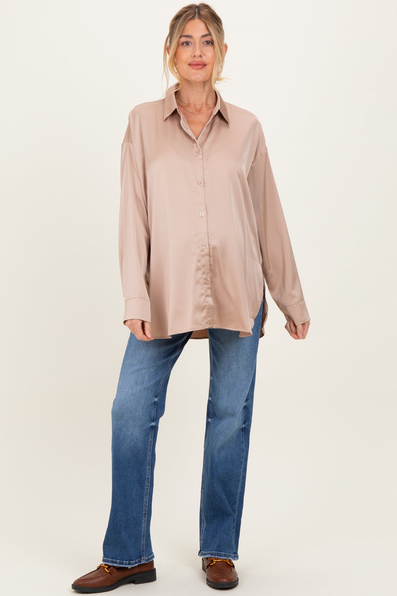 woman wearing a beige satin long sleeve maternity shirt and blue jeans, showing off her baby bump