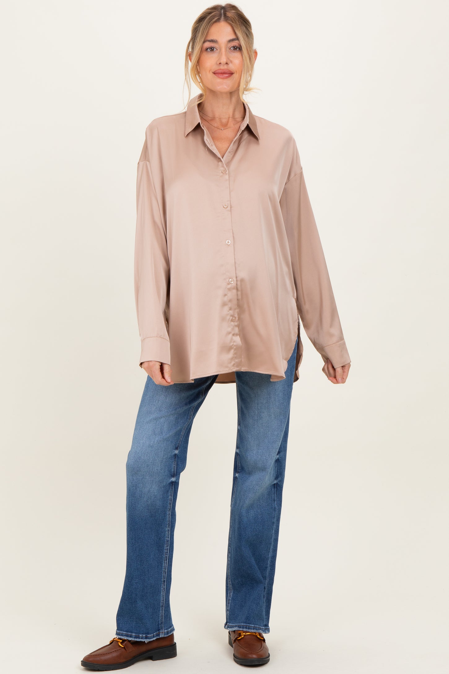woman wearing a beige satin long sleeve maternity shirt and blue jeans, showing off her baby bump