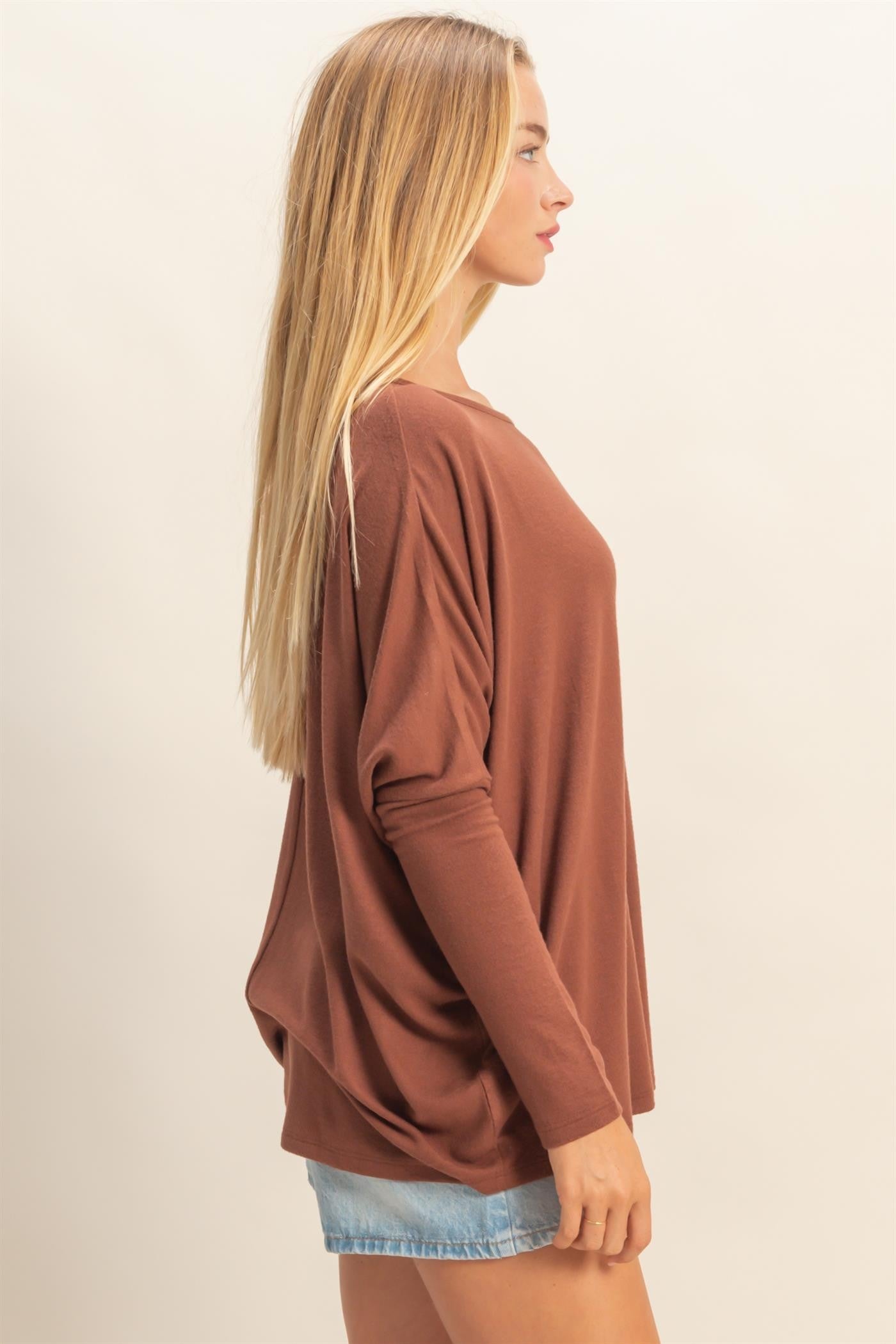 woman wearing a loose-fitting rust brown long sleeve top with a relaxed silhouette and side drape detail