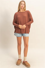 woman wearing a brown oversized long sleeve top with loose sleeves and denim shorts, standing with a relaxed pose