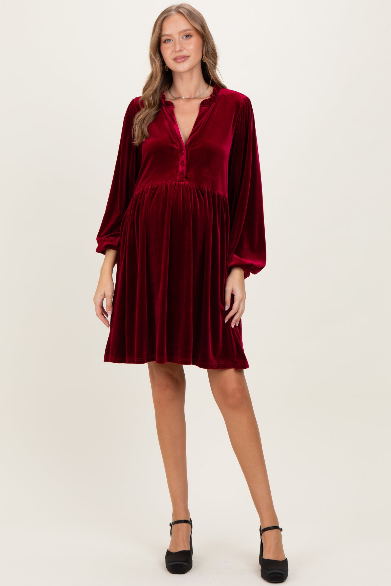 woman wearing a burgundy velvet maternity dress with long sleeves and a button-down neckline, showcasing a baby bump