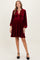 woman wearing a burgundy velvet maternity dress with long sleeves and a button-down neckline, showcasing a baby bump