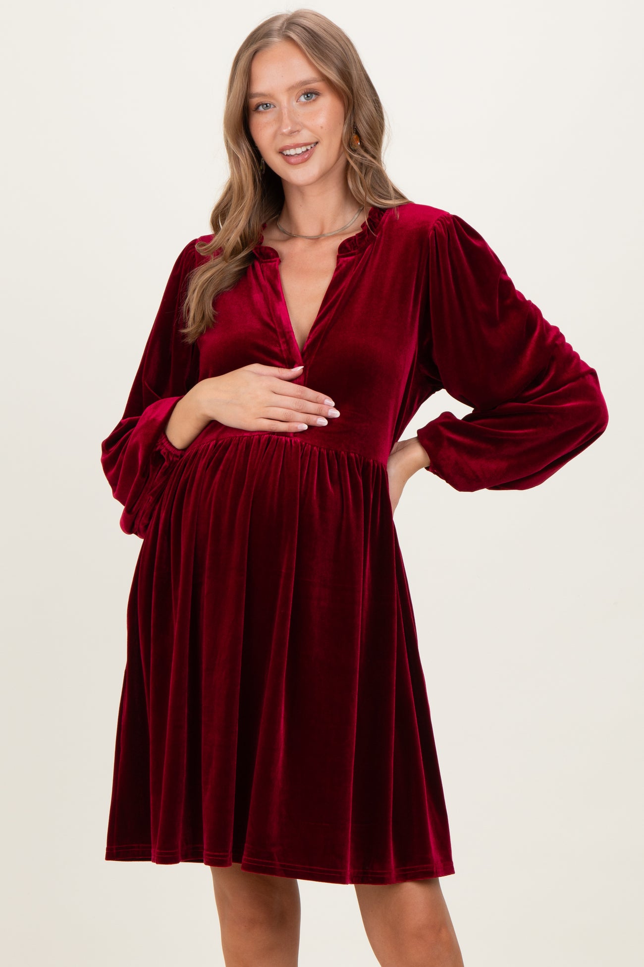 woman wearing a burgundy velvet maternity dress with long sleeves and a v-neck, holding her baby bump