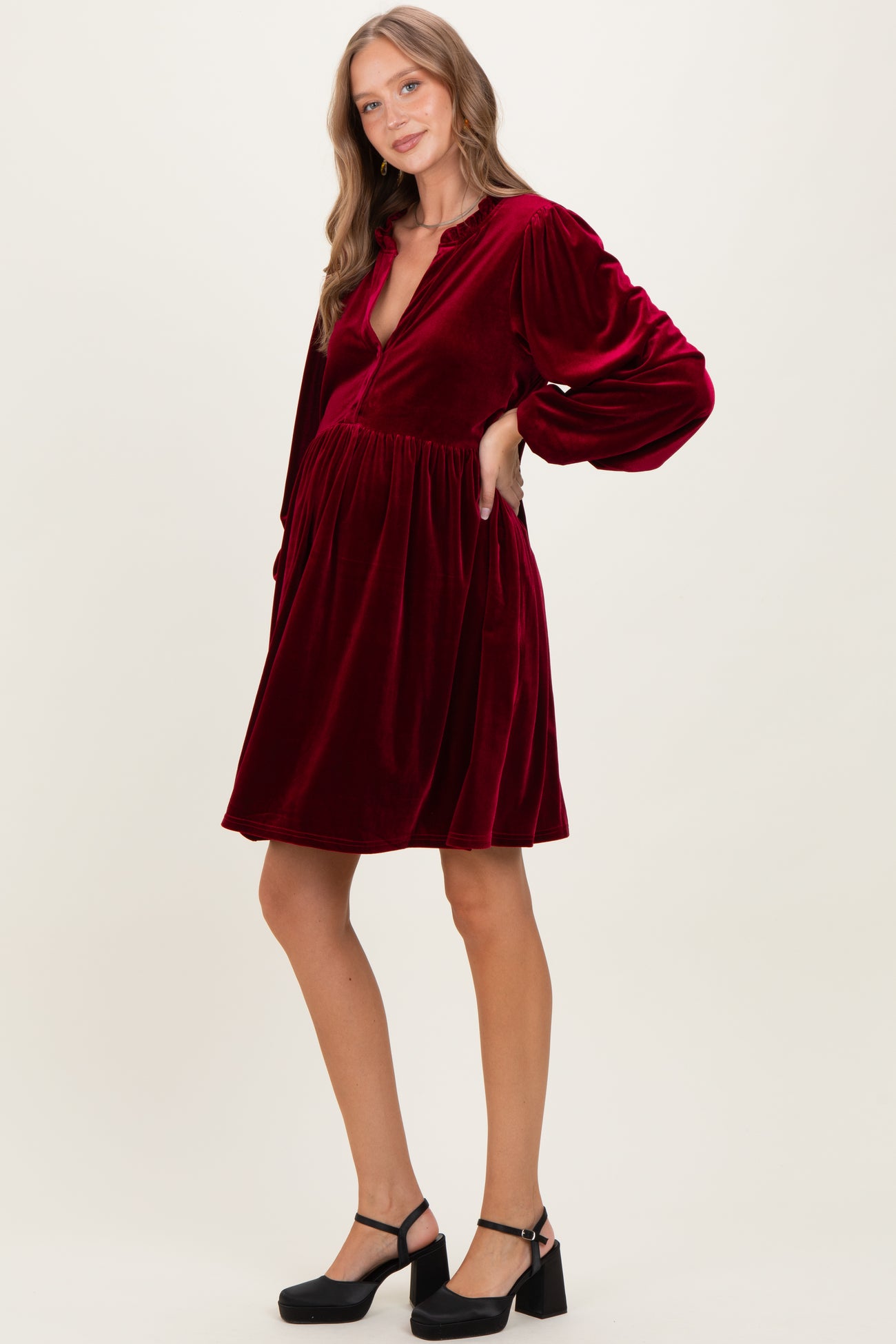woman wearing a burgundy velvet maternity dress with a deep v-neck and long sleeves, showcasing her baby bump