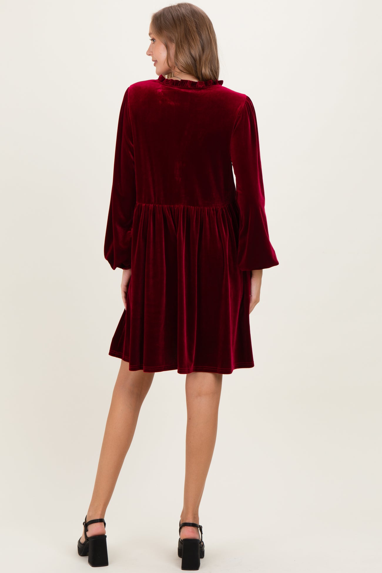 woman wearing a burgundy velvet maternity dress with long sleeves and a flared skirt from the back