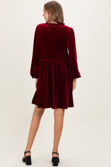woman wearing a burgundy velvet maternity dress with long sleeves and a flared skirt from the back