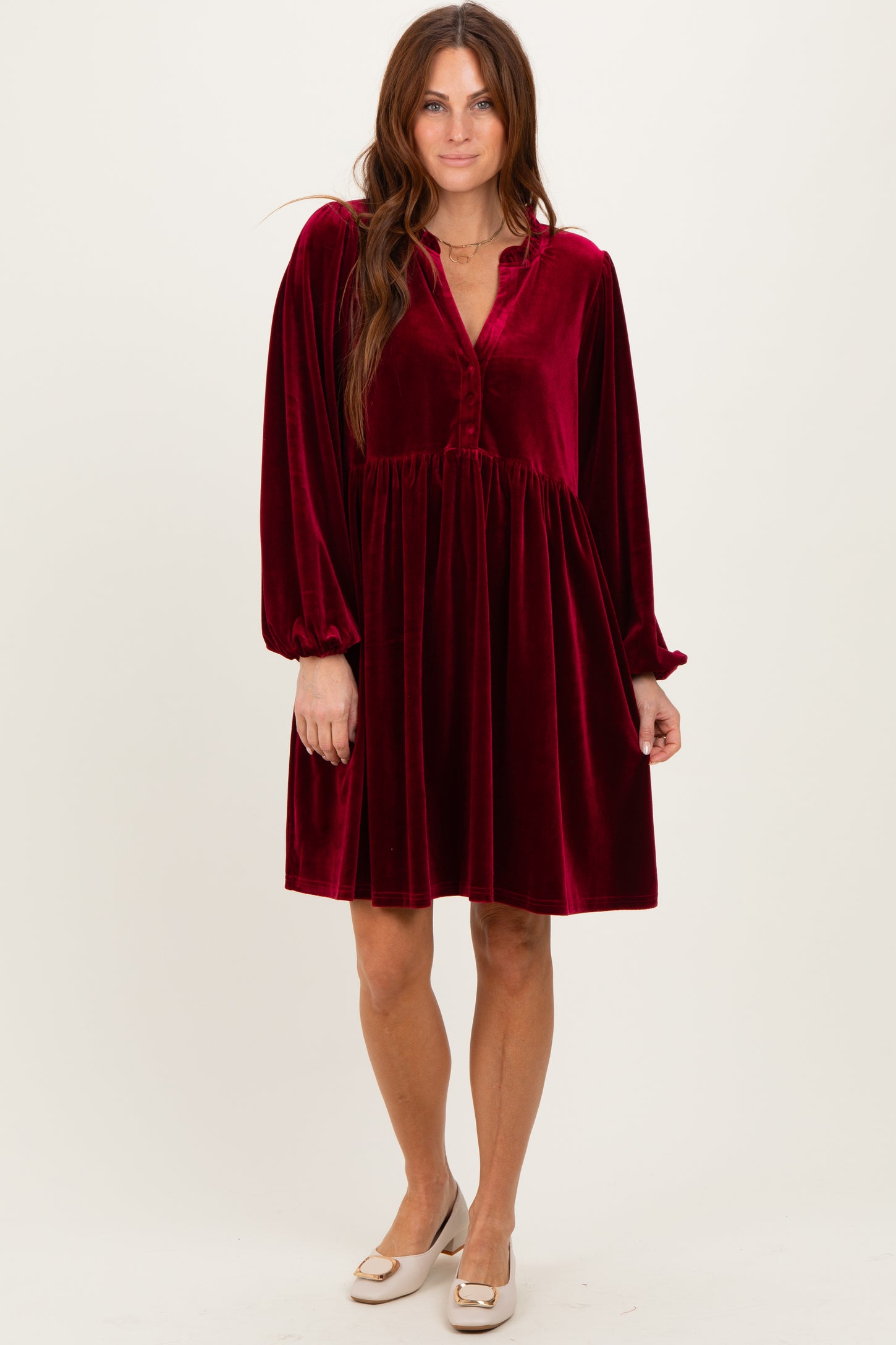 woman wearing a burgundy velvet long sleeve dress with a v-neck and button detailing