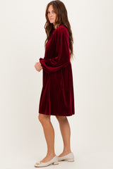 woman wearing a burgundy velvet long sleeve dress with a cinched waist and a relaxed fit