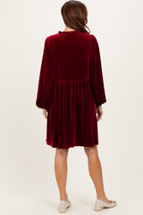 woman wearing a burgundy velvet long sleeve dress with a gathered waist and ruffled neckline, shown from the back