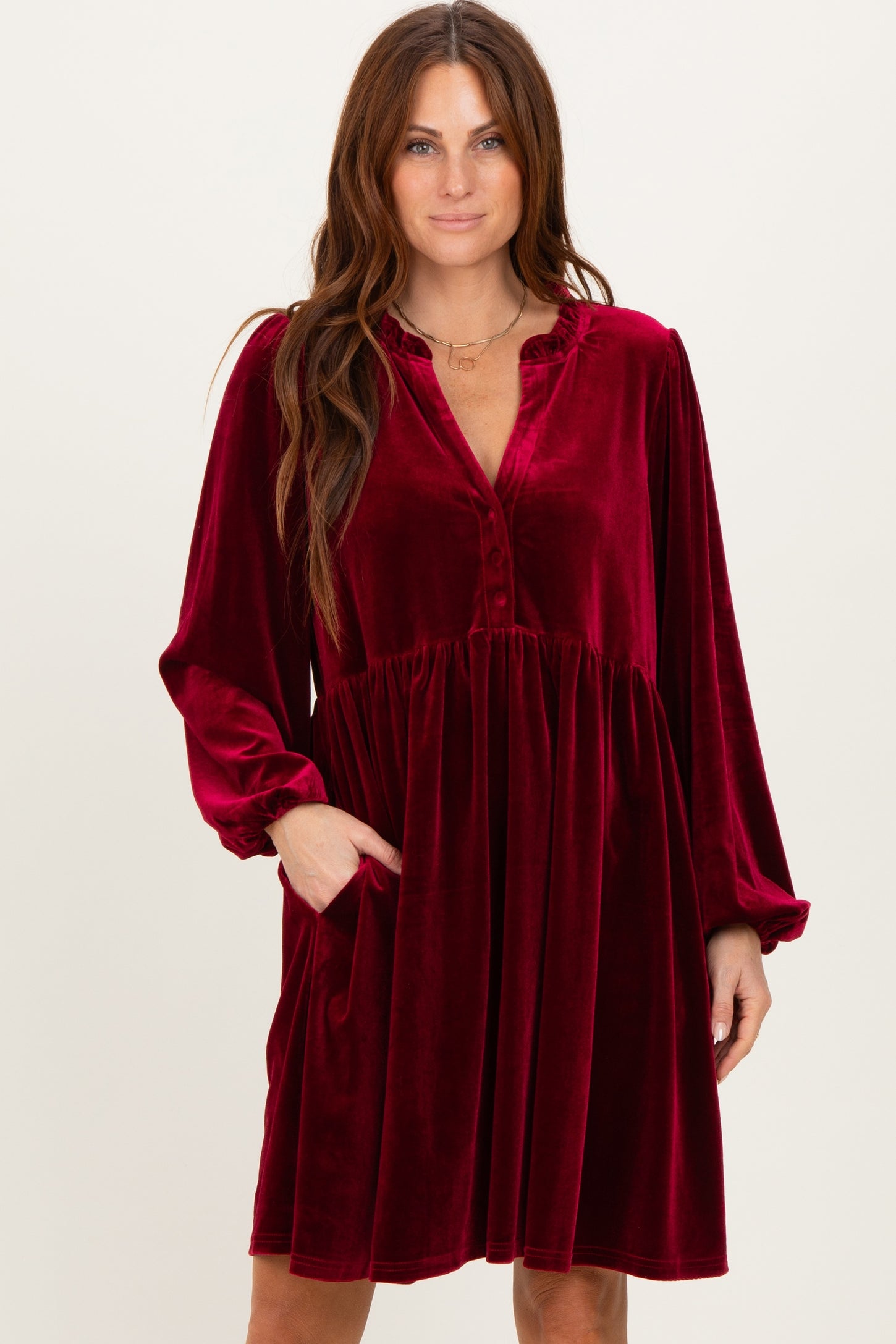 woman wearing a burgundy velvet long sleeve dress with a button front and pockets