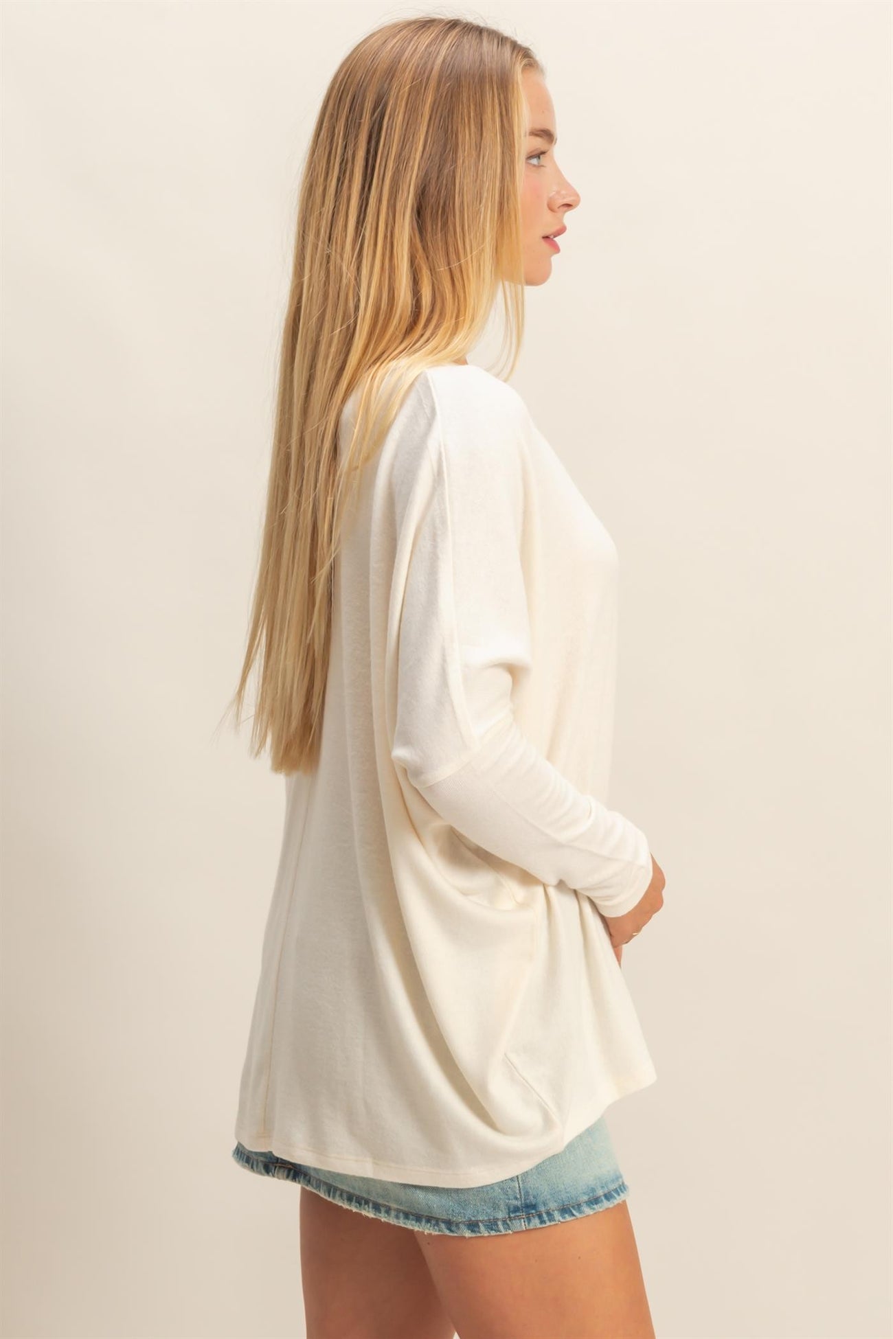 woman wearing a white long sleeve oversized top with a relaxed fit and light blue denim shorts