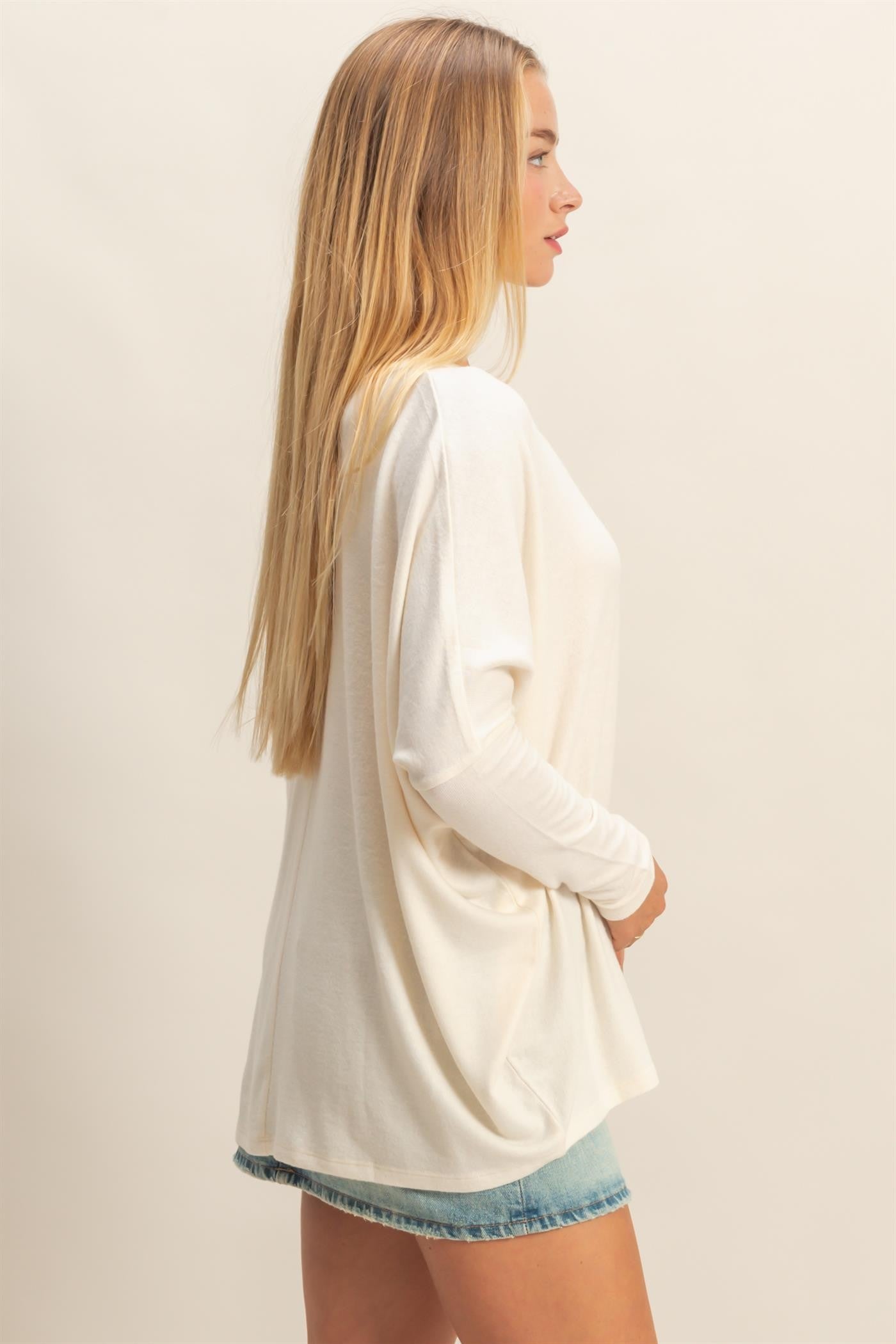woman wearing a white long sleeve oversized top with a relaxed fit and light blue denim shorts