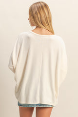 woman wearing an oversized cream sweater with a boat neckline and rolled sleeves, viewed from the back