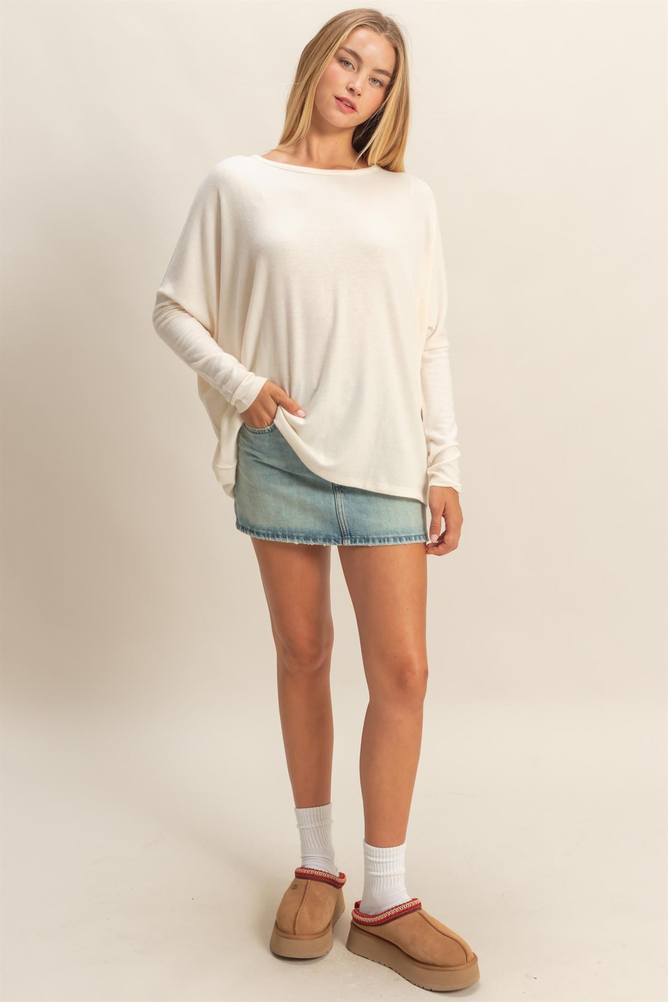 woman wearing a cream oversized sweater with pockets and a denim mini skirt, styled with white socks and brown slip-on shoes