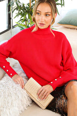 woman wearing a red ribbed turtleneck sweater with button details, holding a straw clutch bag