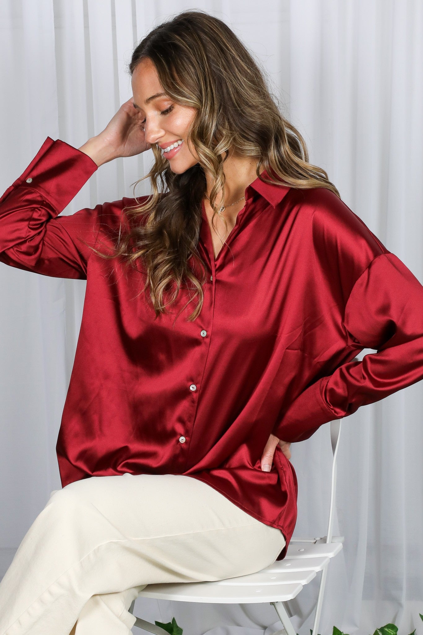 woman wearing a burgundy satin button-up shirt with a relaxed fit and long sleeves, posing with a smile
