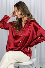 woman wearing a burgundy satin button-up shirt with a relaxed fit and long sleeves, posing with a smile