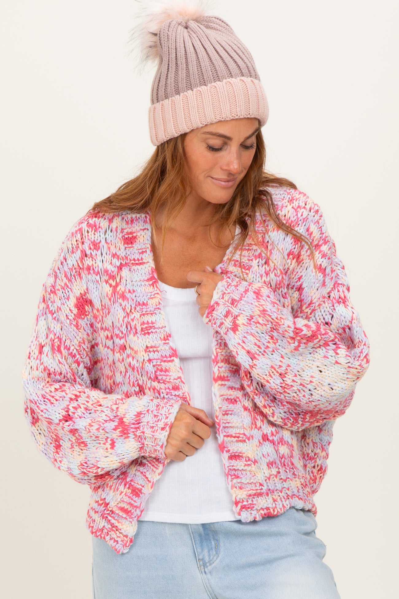 woman wearing a colorful oversized knitted cardigan and a pink beanie, styled with a white tank top and light blue jeans