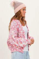 woman wearing a multicolored oversized knit cardigan and a light pink beanie, styled with a white tank top and denim jeans