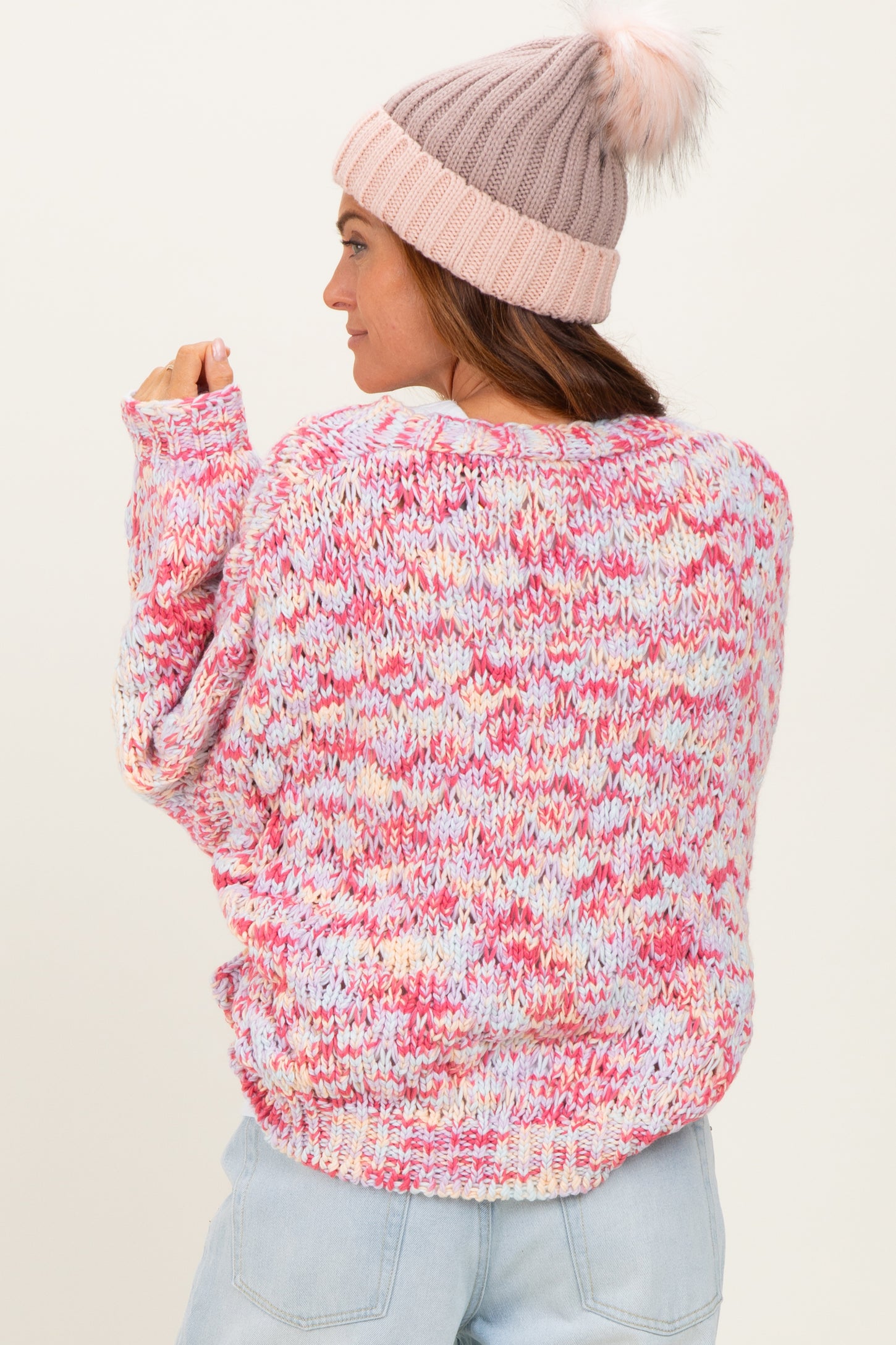 woman wearing a multicolor oversized knit sweater in pastel pink and blue with a soft pink beanie
