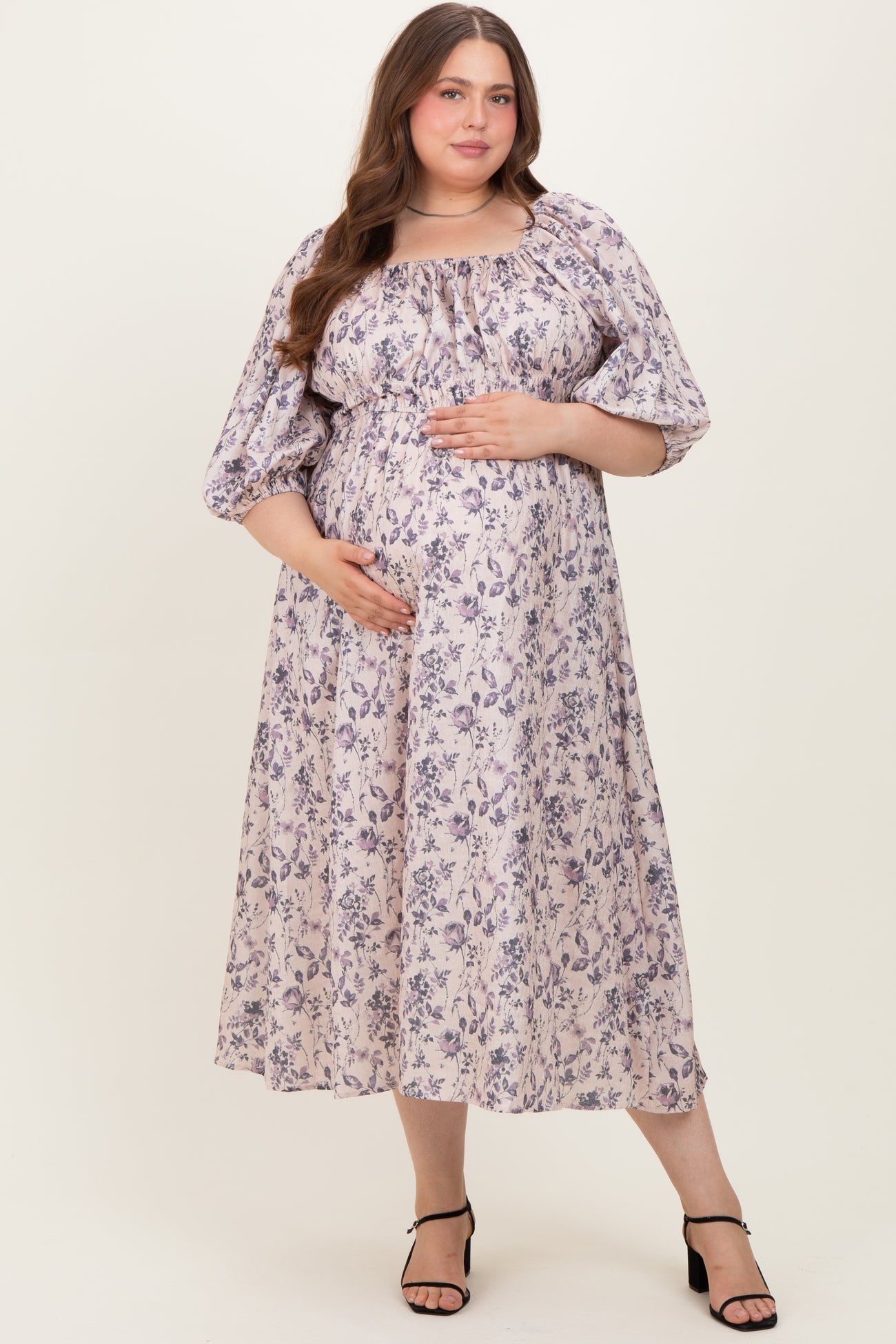 woman wearing a floral print maternity dress with puff sleeves and a baby bump, standing and smiling