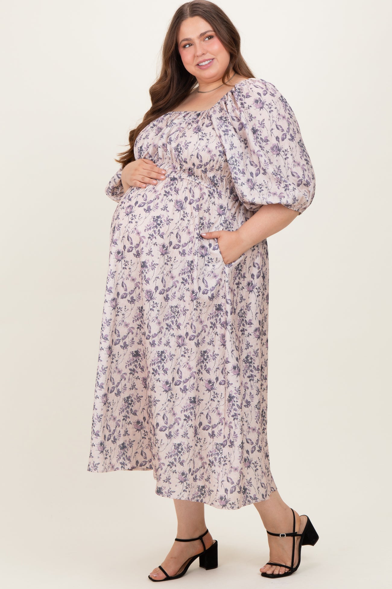 woman wearing a floral print maternity plus maxi dress with puff sleeves and pockets, showing her baby bump