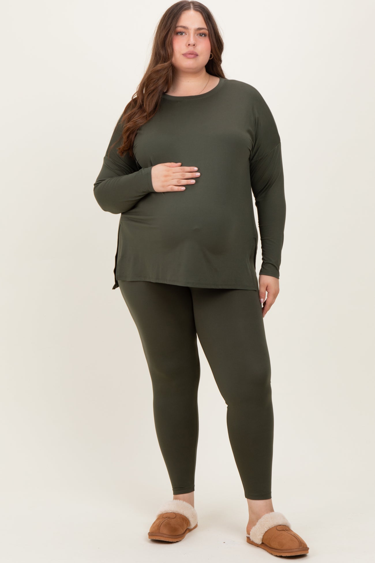 woman wearing a dark green maternity long sleeve top and matching leggings, holding her baby bump