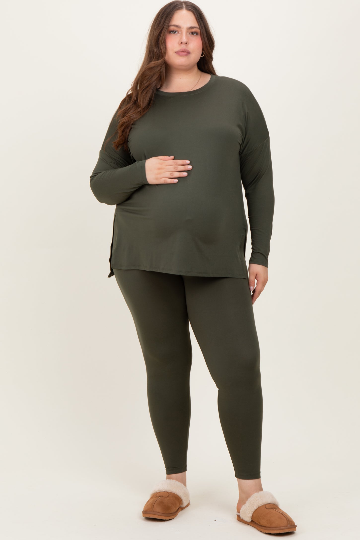 woman wearing a dark green maternity long sleeve top and matching leggings, holding her baby bump