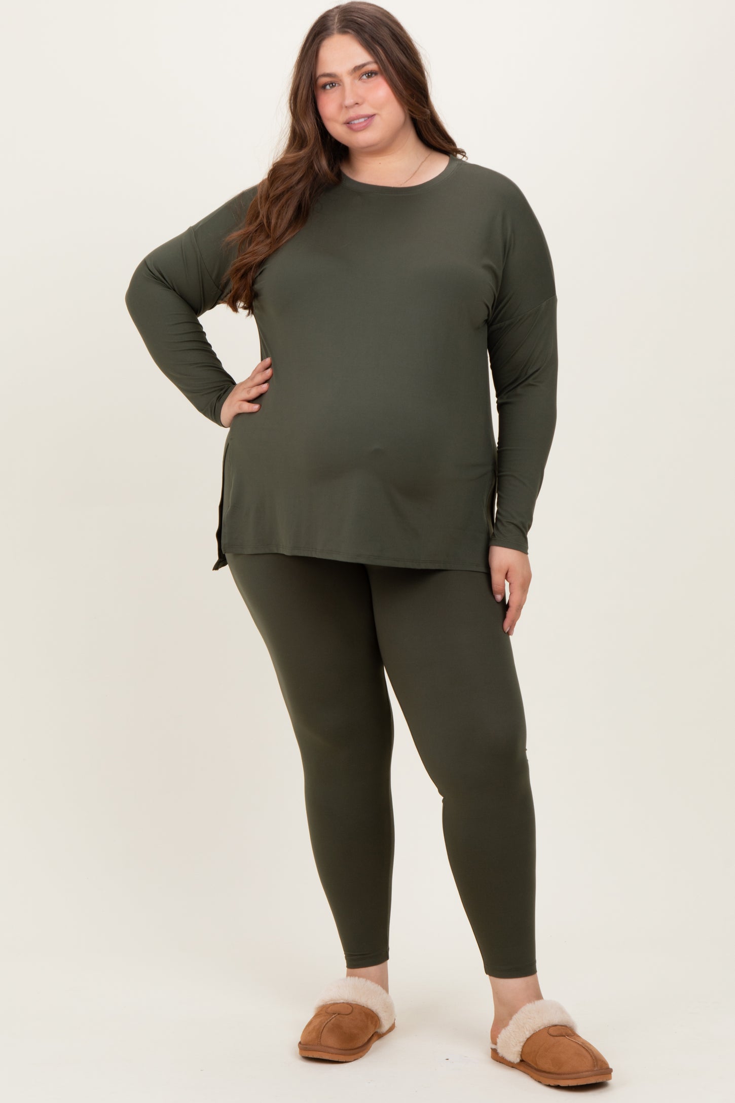 woman wearing a dark green maternity wear long sleeve top and matching leggings, posing with one hand on her hip