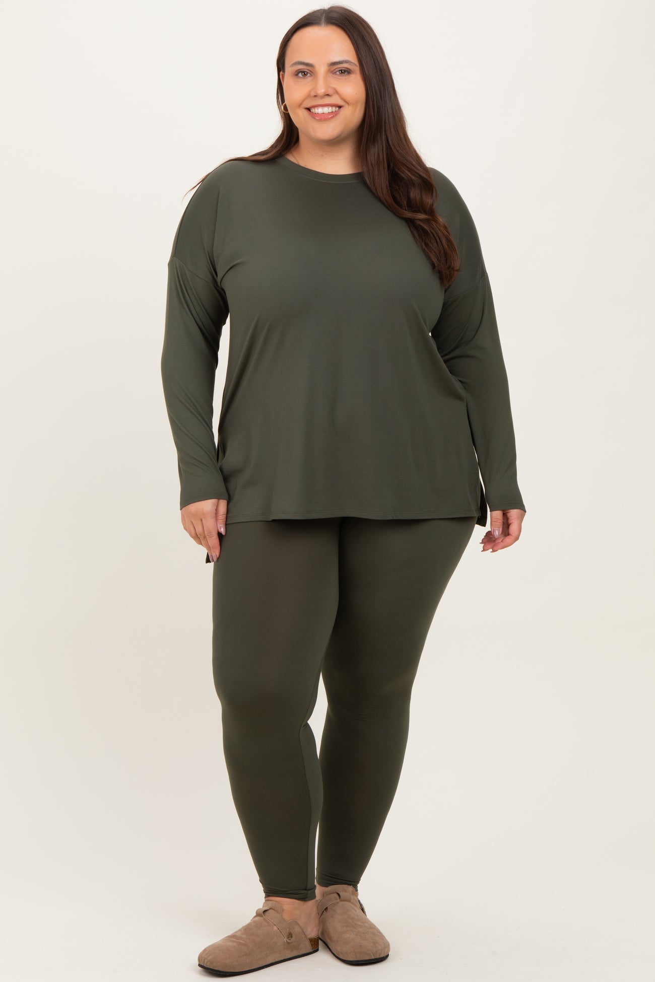 woman in a plus size olive green long sleeve top and matching leggings, standing against a neutral background