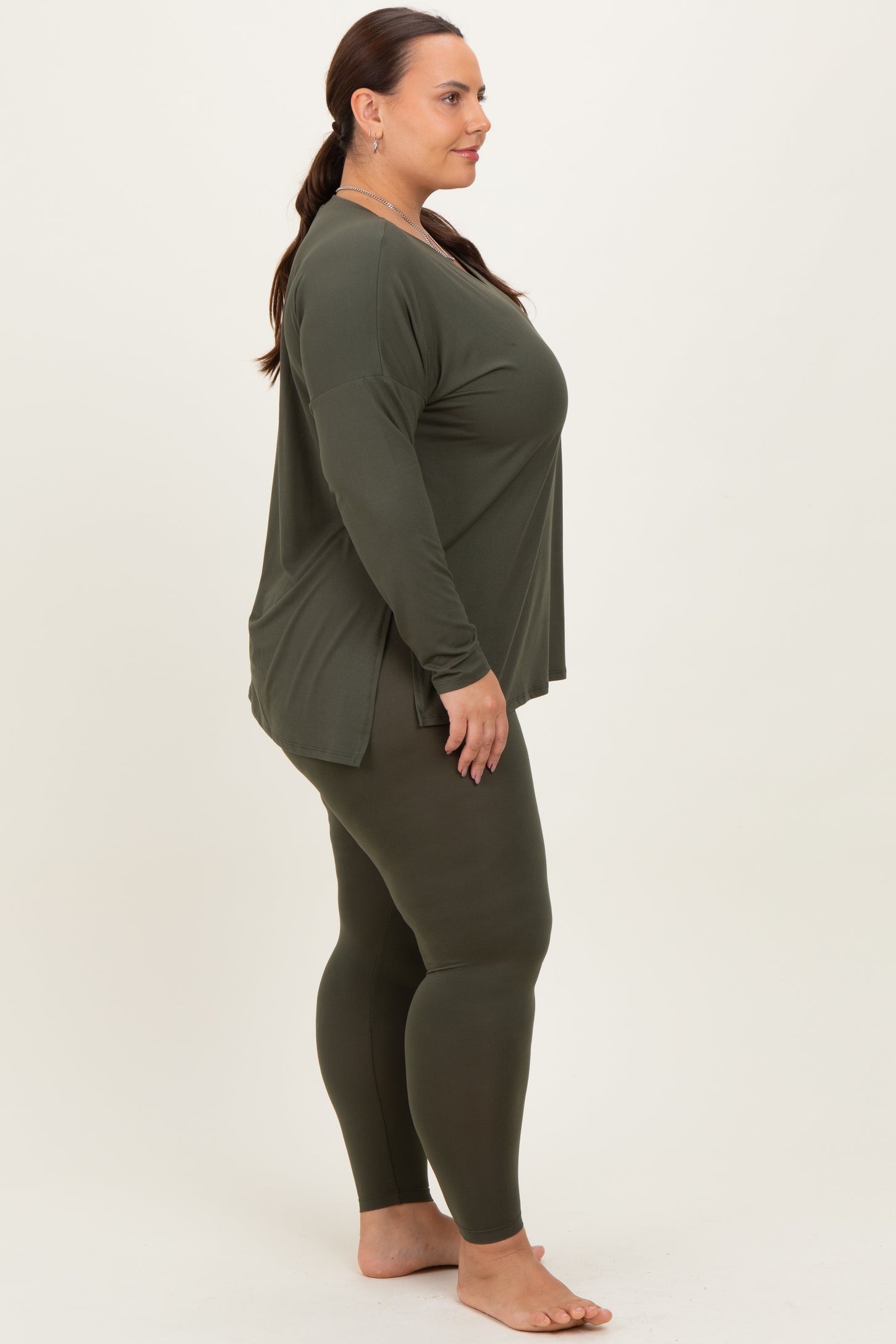 woman wearing a dark olive green oversized long sleeve top and matching leggings, standing in profile