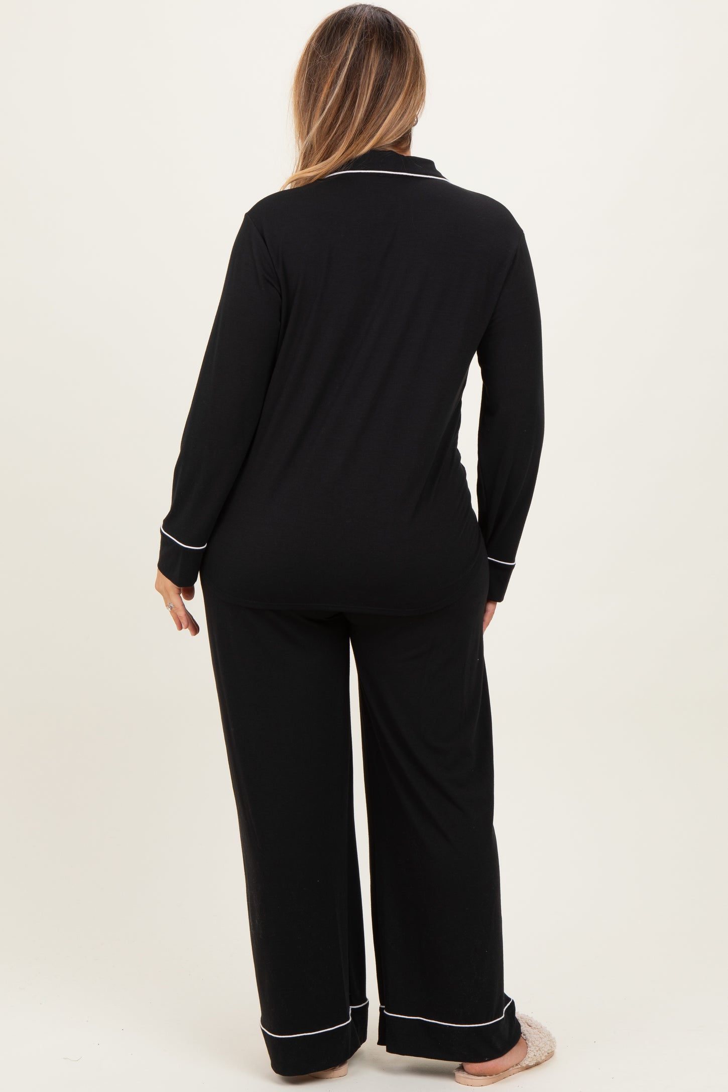 woman wearing a black long sleeve maternity plus pajama set with white piping, showing the back view
