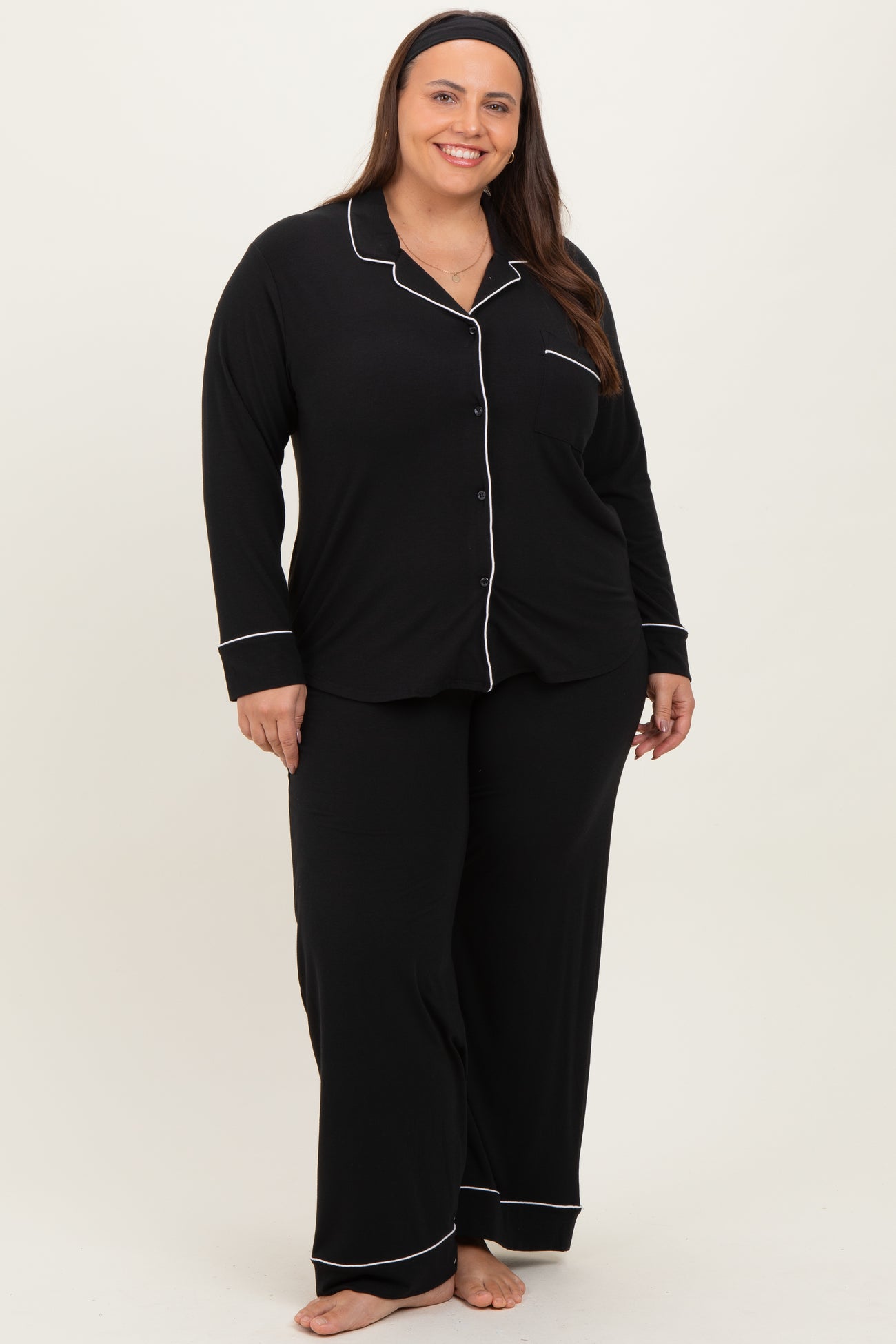 woman wearing a black plus size pajama set with white piping, featuring a button-up top and matching pants