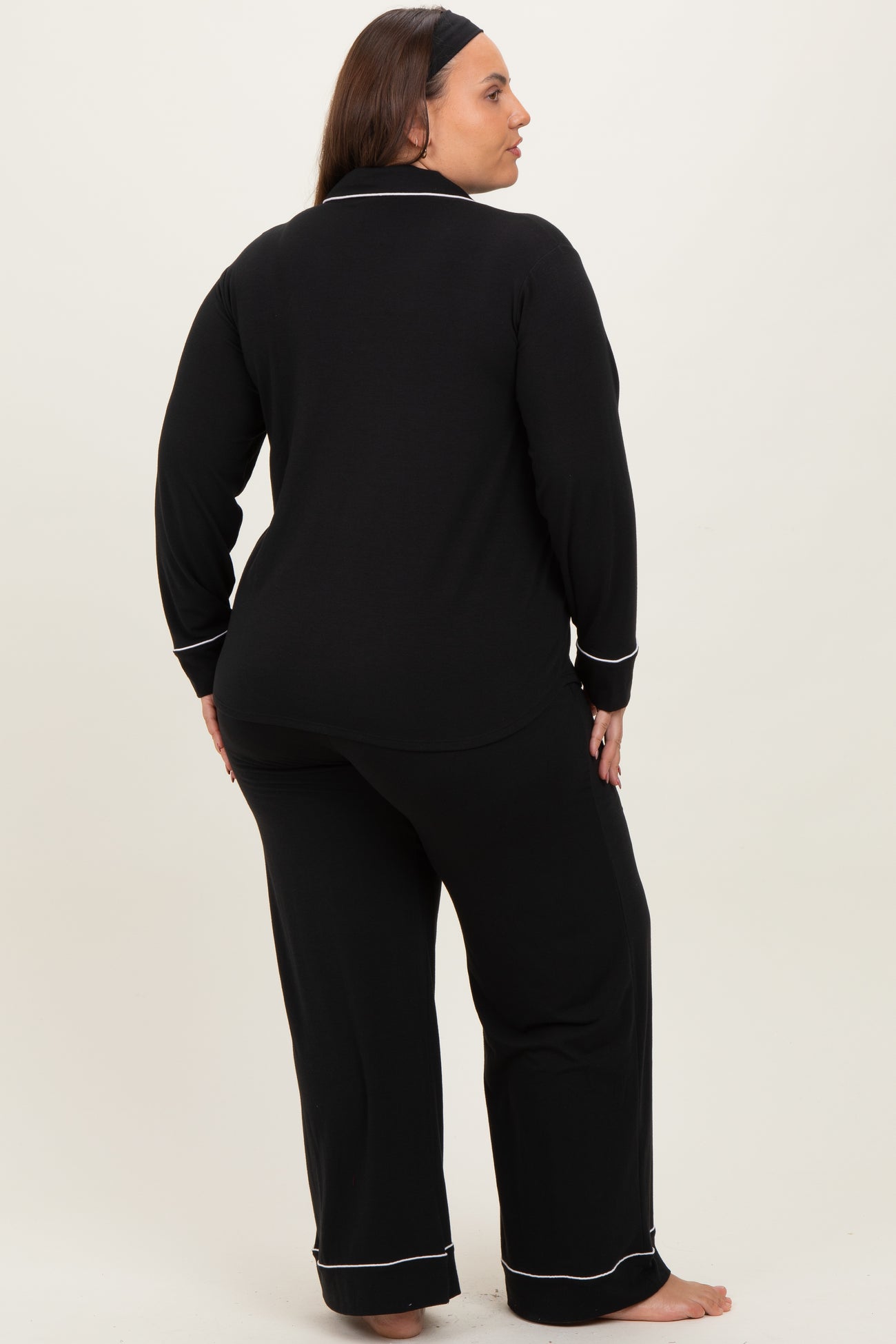woman wearing a black long sleeve pajama set with white piping details, shown from the back